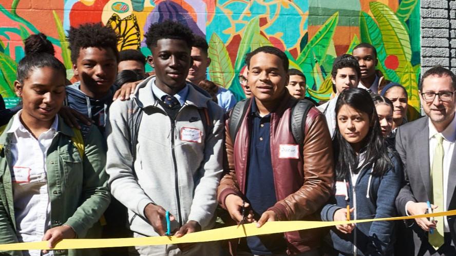 Community leaders, students, and partners gather for a ribbon-cutting ceremony in front of a vibrant mural, celebrating the launch of a new initiative.